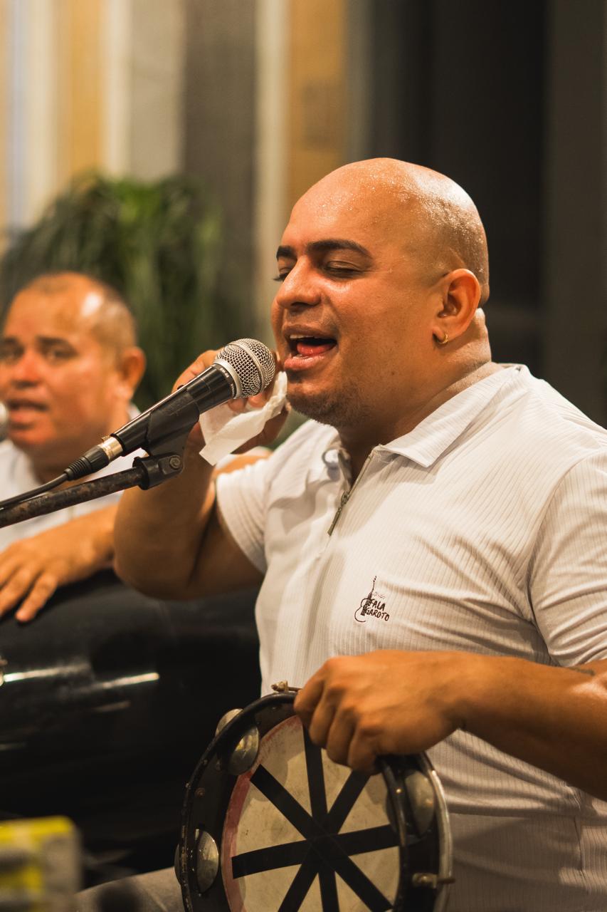 Vocalista do Fala Garoto com pandeiro na mão, cantando ao microfone